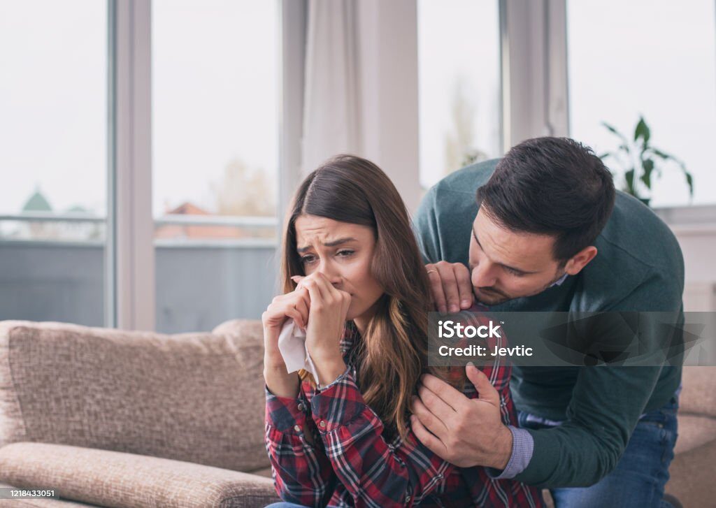 Man consoling sad girl at home with hug and his presence